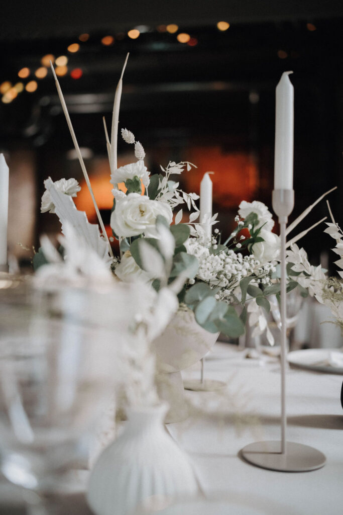 Ein komplett weiß gedeckter Tisch mit Kerzen und weißen rosen grünem Gewächs.